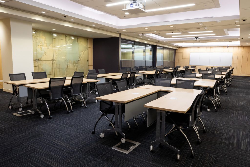 Conference Room 1ABC at One Rotary Place. Photo of a large conference room with tables &amp; chairs, a whiteboard, a projector, and screen.