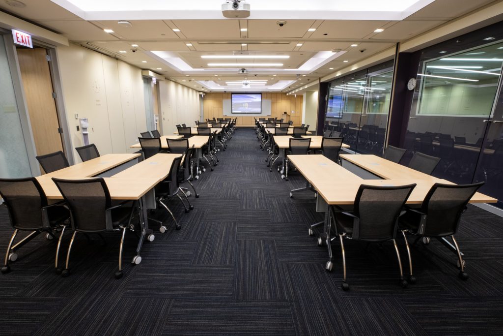 Conference Room 1ABC at One Rotary Place. Photo of a large conference room with tables &amp; chairs, a whiteboard, a projector, and screen.