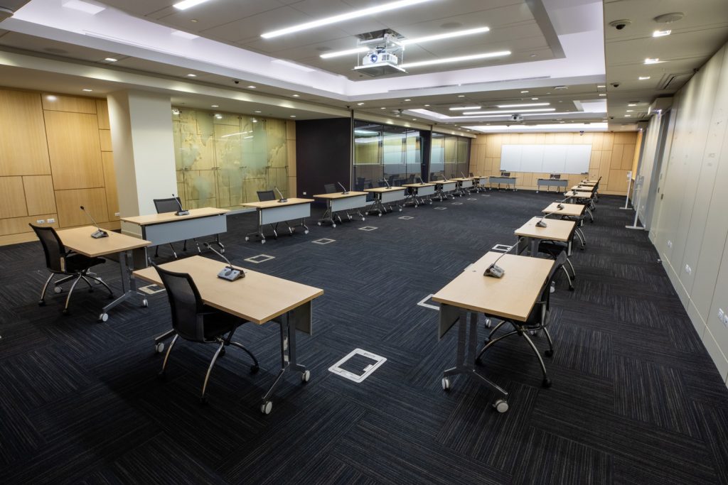 Conference Room 1ABC at One Rotary Place. Photo of a large conference room with tables &amp; chairs, a whiteboard, a projector, and screen.
