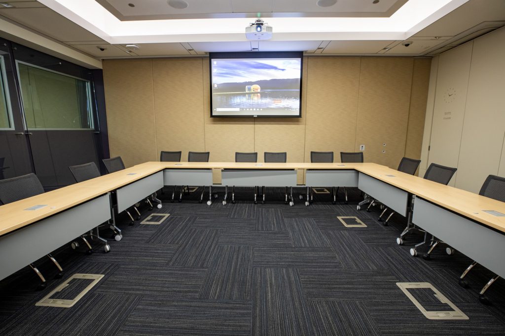 Conference Room 1B at One Rotary Place. Photo of a large conference room with tables &amp; chairs, a projector, and screen.