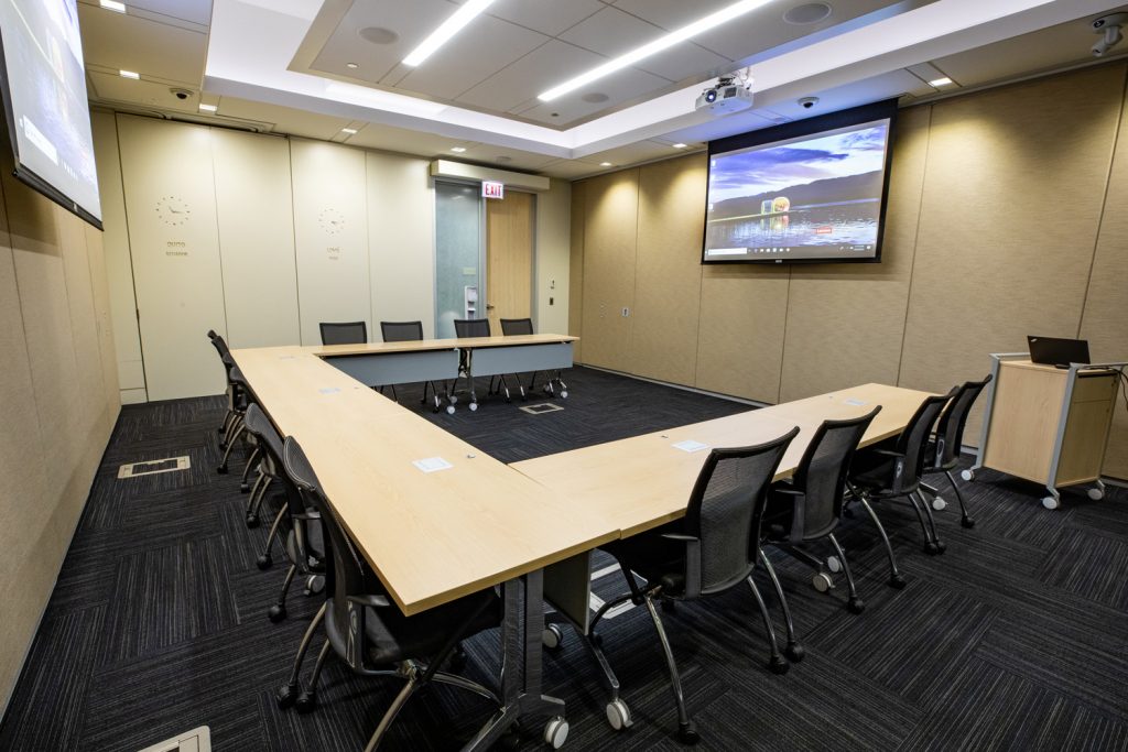 Conference Room 1B at One Rotary Place. Photo of a large conference room with a podium &amp; laptop, a projector, and screen.