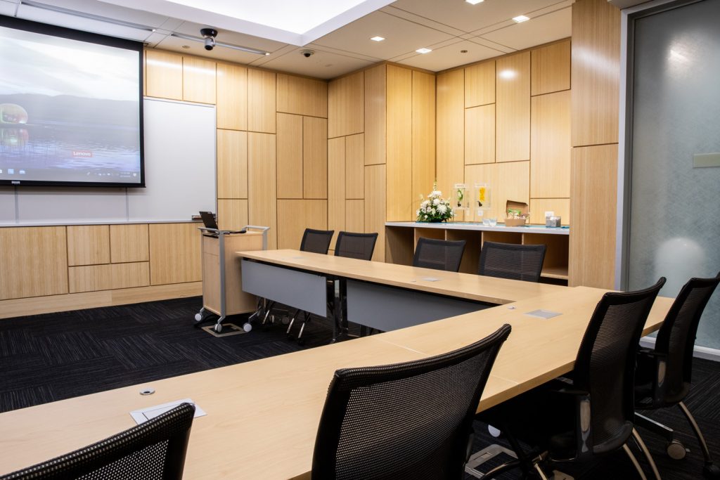 Conference Room 1C at One Rotary Place. Photo of a large conference room with a podium, tables &amp; chairs, a projector, and screen.
