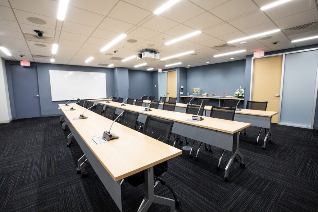 Conference Room 3A at One Rotary Place. Photo of a large conference room with tables &amp; chairs, a projector, and a whiteboard.