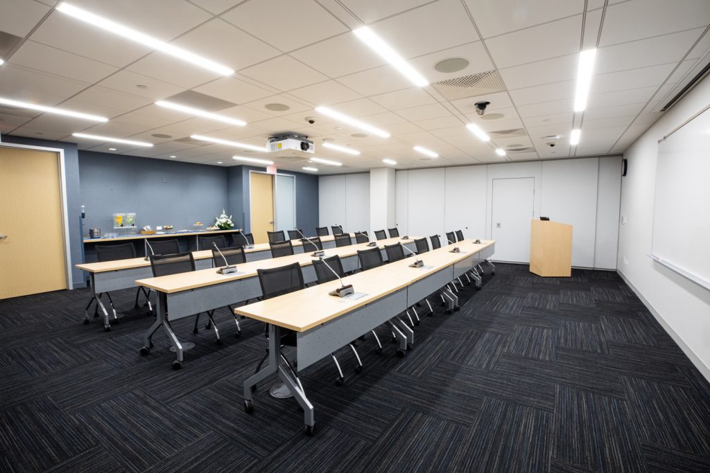 Conference Room 3A at One Rotary Place. Photo of a large conference room with tables &amp; chairs, a podium, and a whiteboard.
