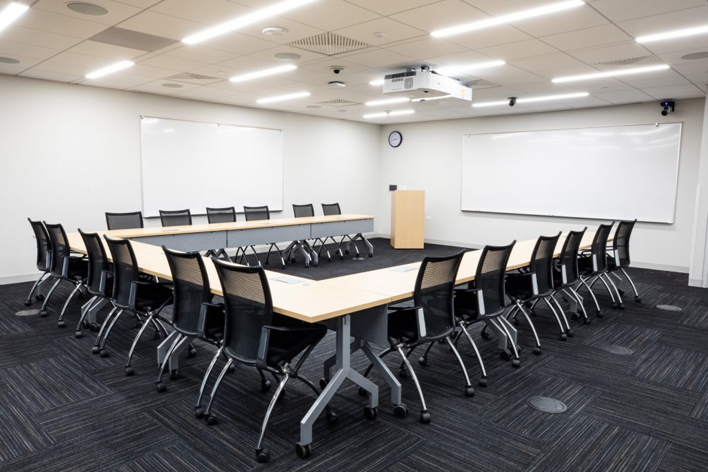 Conference Room 3B at One Rotary Place. Photo of a large conference room with tables &amp; chairs, a podium, projector, and multiple whiteboards.