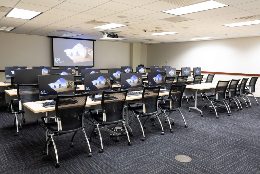 3W Conference Room at One Rotary Place. Photo of a large conference room with tables &amp; chairs, computer stations, a projector, and screen.